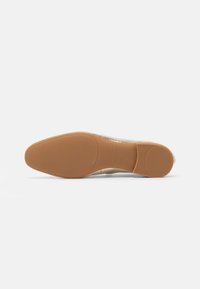 Beige shoe sole with a smooth, matte finish, featuring a rounded toe shape and a flat, rubberized lower material with brand detailing.