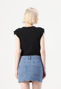 Top negro de manga corta combinado con una mini falda de denim azul claro, que presenta bolsillos traseros y una cintura ajustada, exhibiendo un diseño limpio.
