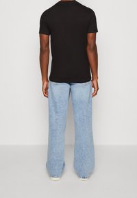 Černé bavlněné tričko s krátkým rukávem spárované se světle modrými džíny rovného střihu s vybledlým vzhledem a roztrhanými okraji.