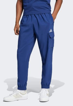 Navy blue athletic pants made of smooth fabric, featuring an elastic waistband, cuffed ankles, and a side cargo pocket with logo detail.
