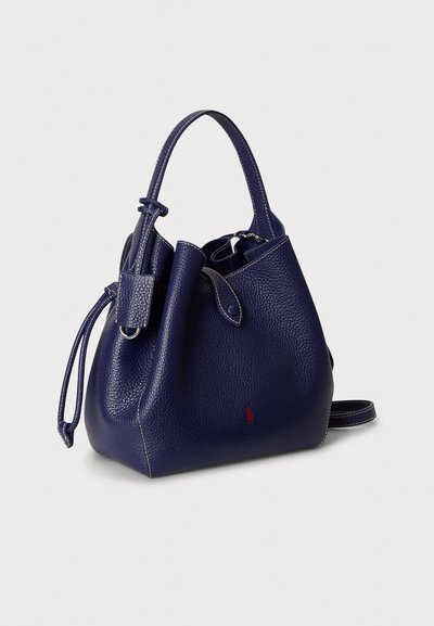 Laivastonsininen nahkainen säilytyskassi teksturoidulla pinnalla, yhdellä yläkahvalla, säädettävällä olkahihnalla ja punaisella logokoristeella. Sisältää nyörikiinnityksen.