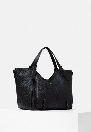 Borsa a mano in pelle nera strutturata con doppi manici, dettagli con cerniere e motivi in rilievo sottili su sfondo bianco.