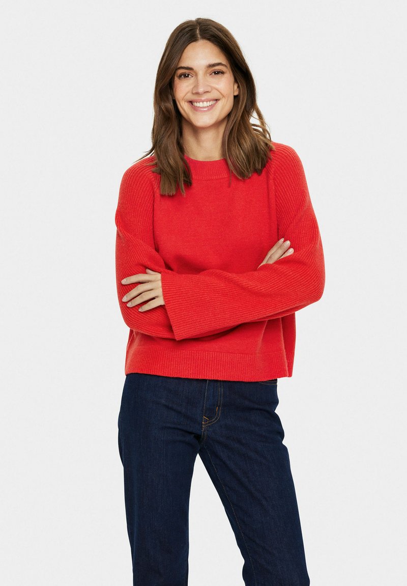 Maglione rosso a maglia con una vestibilità comoda, spalle scese e tessuto a coste. Abbinato a jeans di denim blu scuro.