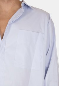 Camicia a righe azzurro chiaro con colletto, taschino singolo sul petto e tessuto morbido. Presenta maniche lunghe e una vestibilità rilassata.