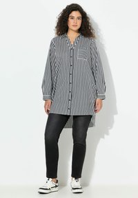 Camicia lunga a righe bianche e nere con chiusura a bottoni sul davanti, maniche lunghe e taschino sul petto. Abbinata a jeans neri aderenti e sneaker.