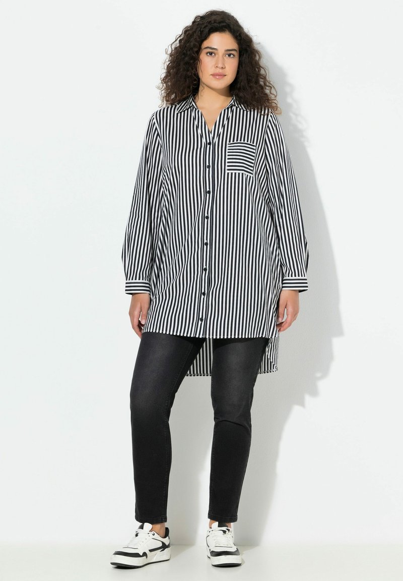 Camicia lunga a righe bianche e nere con chiusura a bottoni sul davanti, maniche lunghe e taschino sul petto. Abbinata a jeans neri aderenti e sneaker.