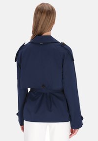 Marineblauwe trenchcoat met een tailleceintuur, knoopdetails en een cropped achterkant. Zachte stof met een klassieke kraag en lange mouwen.