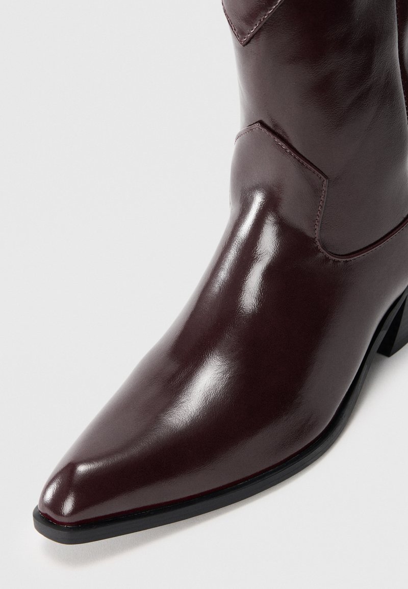 Stivale alla caviglia in pelle borgogna con punta affilata, texture liscia, cuciture sottili e tacco nero. Presenta una silhouette elegante.