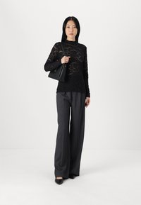 Black lace long-sleeve top with floral pattern, paired with dark gray wide-leg trousers and black handbag. Pointed toe flats complete the outfit.