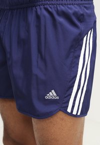 Námořnické modré sportovní šortky vyrobené z hladké tkaniny, které mají bílé akcentové pruhy a vyšívané logo. Elastický pás pro lepší přilnutí.