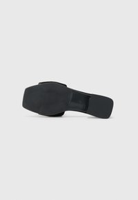 Black flat-soled shoe with a smooth texture. Features a square toe and minimalistic design. Sole is sturdy with subtle grip detailing.