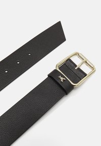 Cintura in pelle nera, finitura testurizzata, fibbia in metallo color oro, estremità appuntita, multiple perforazioni per la regolazione, piccolo emblema decorativo vicino alla fibbia.
