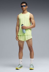 Αθλητική μπλούζα χωρίς μανίκια σε χρώμα φωτεινό πράσινο λάιμ και αντίστοιχα σορτς, συνοδευόμενα από μπλε γυαλιά ηλίου και ανοιχτό μπλε παγούρι. Αθλητικά παπούτσια με κίτρινες λεπτομέρειες.