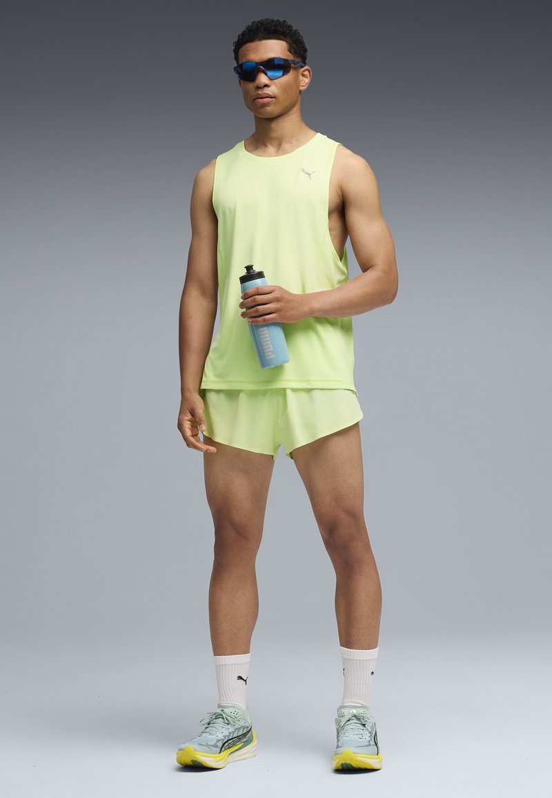 Αθλητική μπλούζα χωρίς μανίκια σε χρώμα φωτεινό πράσινο λάιμ και αντίστοιχα σορτς, συνοδευόμενα από μπλε γυαλιά ηλίου και ανοιχτό μπλε παγούρι. Αθλητικά παπούτσια με κίτρινες λεπτομέρειες.