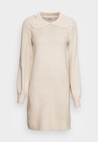 Abito di maglione lavorato a maglia color crema con un ampio colletto, maniche lunghe, polsini a coste e una vestibilità rilassata. Realizzato in un morbido materiale con una superficie texturizzata.