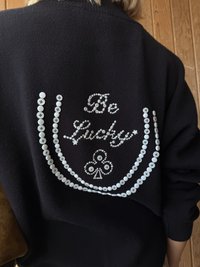 Czarny sweter z ozdobnymi białymi guzikami i cyrkoniami. Napis "Be Lucky" z symbolem serca i karo, ułożony w zakrzywiony wzór.