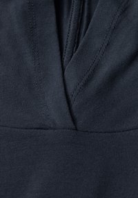 Tejido azul marino oscuro con una textura suave y lisa. Presenta un diseño de escote en V y detalles cosidos a lo largo de los bordes. Vista en primer plano del material.