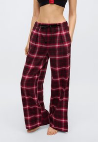 Κόκκινο και μαύρο καρό παντελόνι πιτζάμας με φαρδιά εφαρμογή, ελαστική μέση με κορδόνι και απαλή υφή υφάσματος. Το λογότυπο της μάρκας είναι ορατό στο πόδι.