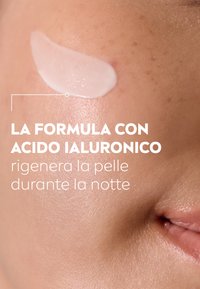 Crema bianca che scivola su una superficie della pelle di color marrone chiaro, evidenziando una texture liscia con sottili imperfezioni naturali della pelle.