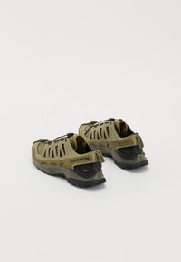 Green mesh and rubber outdoor shoes with black accents, featuring a slip-on design, adjustable laces, and a textured sole for grip.