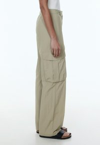 Beige cargo broeken met een relaxed fit, gemaakt van lichtgewicht materiaal. Voorzien van zijzakken en een gecropt model, gecombineerd met donkere sandalen.