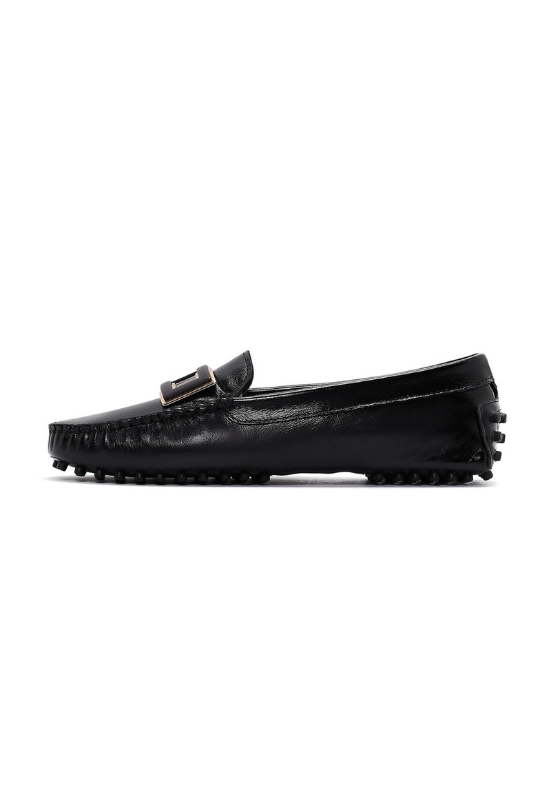 Mocassins en cuir noir avec une semelle plate, dotés d'une boucle décorative et de coutures visibles sur le dessus. Semelle extérieure avec une texture antidérapante.