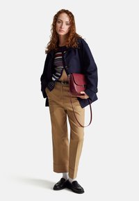 Marineblauwe cropped jacket, gestreepte gebreide top, tankleurige broeken met opgerolde mouwen, zwarte loafers en een kastanjebruine schoudertas met een gestructureerde afwerking.