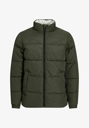 Zöld párnázott dzseki magas gallérral, elől cipzárral és rugalmas mandzsettákkal, sötét farmernadrággal és fekete-fehér tornacipővel párosítva.