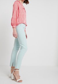 Blusa rossa con motivo e maniche a sbuffo abbinata a pantaloni slim-fit azzurri chiari con spacchi laterali. Sandali bianchi con tacco completano l'outfit.