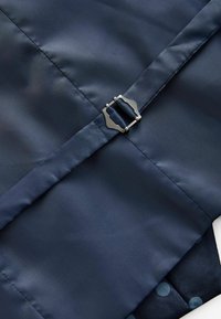 Marineblauter Stoff mit glatter Textur besitzt einen metallischen Verschluss. Darunter ist ein gemusterter Textil mit blauen Punkten und vertikalen Streifen sichtbar.