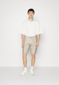 Jasny bawełniany t-shirt z krótkim rękawem, zestawiony z beżowymi szortami z pasem na sznurku. Całość dopełniają białe sneakersy.