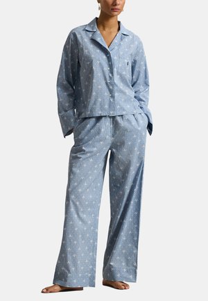 Femme portant un ensemble pyjama rayé bleu clair avec de petits motifs floraux blancs, manches longues, haut boutonné et pantalon à jambes larges.