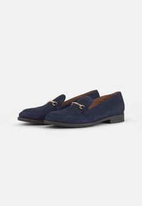 Tumedat sinised nahast slip-on kingad, millel on veidi ümar varvas, dekoratiivne kuldne aksessuaar ja madal laotud konts.