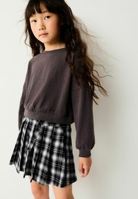 Grau langer Pullover mit gerafftem Saum, kombiniert mit einem schwarz-weißen karrierten Faltenrock. Strukturiertes Material, lässige Passform.