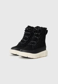 Bottes de cheville en suède noir avec des semelles épaisses blanches contrastantes, accentuées par des lacets noirs et une douce bordure en fausse fourrure en haut.