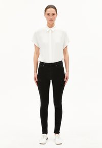 Camisa blanca de manga corta con cuello recto, combinada con jeans skinny negros y zapatos blancos. Diseño sencillo, textura suave.