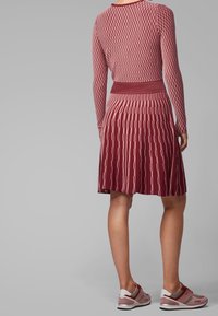 Robe en tricot rouge avec un motif texturé, manches longues et taille cintrée. Associée à des chaussures de sport grises et roses avec des accents blancs.