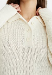 Crèmekleurige gebreide pullover met een kraag, een knoopsluiting met drie grote knopen, geribbelde manchetten en een gestructureerd patroon.