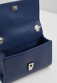 Sac à main texturé bleu marine avec rabat à l'avant, quincaillerie en argent et fermeture à bouton magnétique. L'intérieur comprend un seul compartiment.