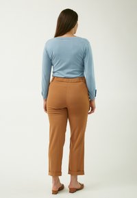 Hellblaues Langarmshirt mit rundem Halsausschnitt, kombiniert mit beigen, schmal zulaufenden Hosen mit elastischem Bund und umgeschlagenen Säumen. Schlichtes Design.