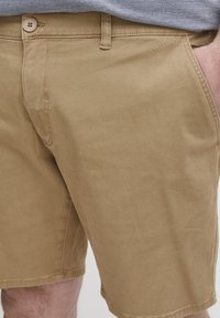 Helle, beige Shorts aus Baumwoll-Twille, mit einem Knopfverschluss, seitlichen Taschen und einem sauberen Saum mit subtiler Textur.