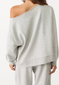 Lichtgrijze, oversized sweatshirt met een brede halslijn, lange mouwen en geribbelde boorden. Zachte textuur, getoond op de rug van een model.