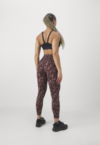 Sujeta deportiva negra con tirantes ajustables combinada con leggings de talle alto en color burdeos con un patrón abstracto ligero. Zapatillas deportivas negras.