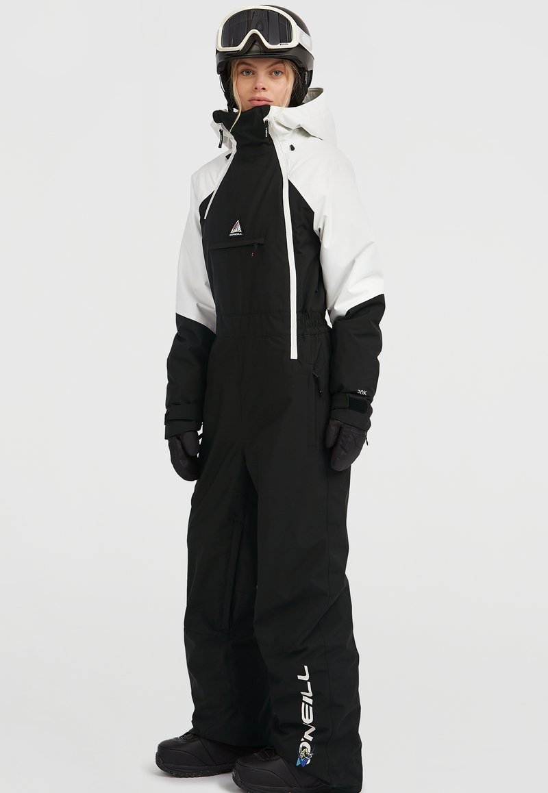 Traje de esquí en blanco y negro con bolsillos con cremallera, puños elásticos y un cuello alto. Incluye un logotipo en la pierna del pantalón y se combina con un casco.
