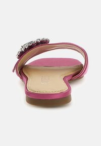 Sandalo slide in raso rosa con un logo decorativo argentato sulla fascia, dotato di suola piatta e design con apertura sul retro.