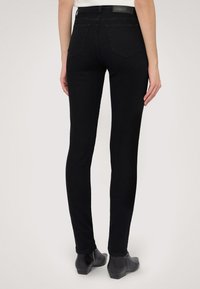 Schwarze, schmal geschnittene Jeans aus Denim mit hoher Taille, zwei Gesäßtaschen und einer glatten Textur. Tragen mit schwarzen Ankle Boots.