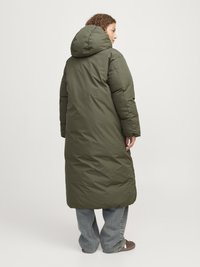 Palton pufos lung de culoare verde măslinie, cu glugă, având o textură netedă și un croi drept. Purtați peste blugi largi.