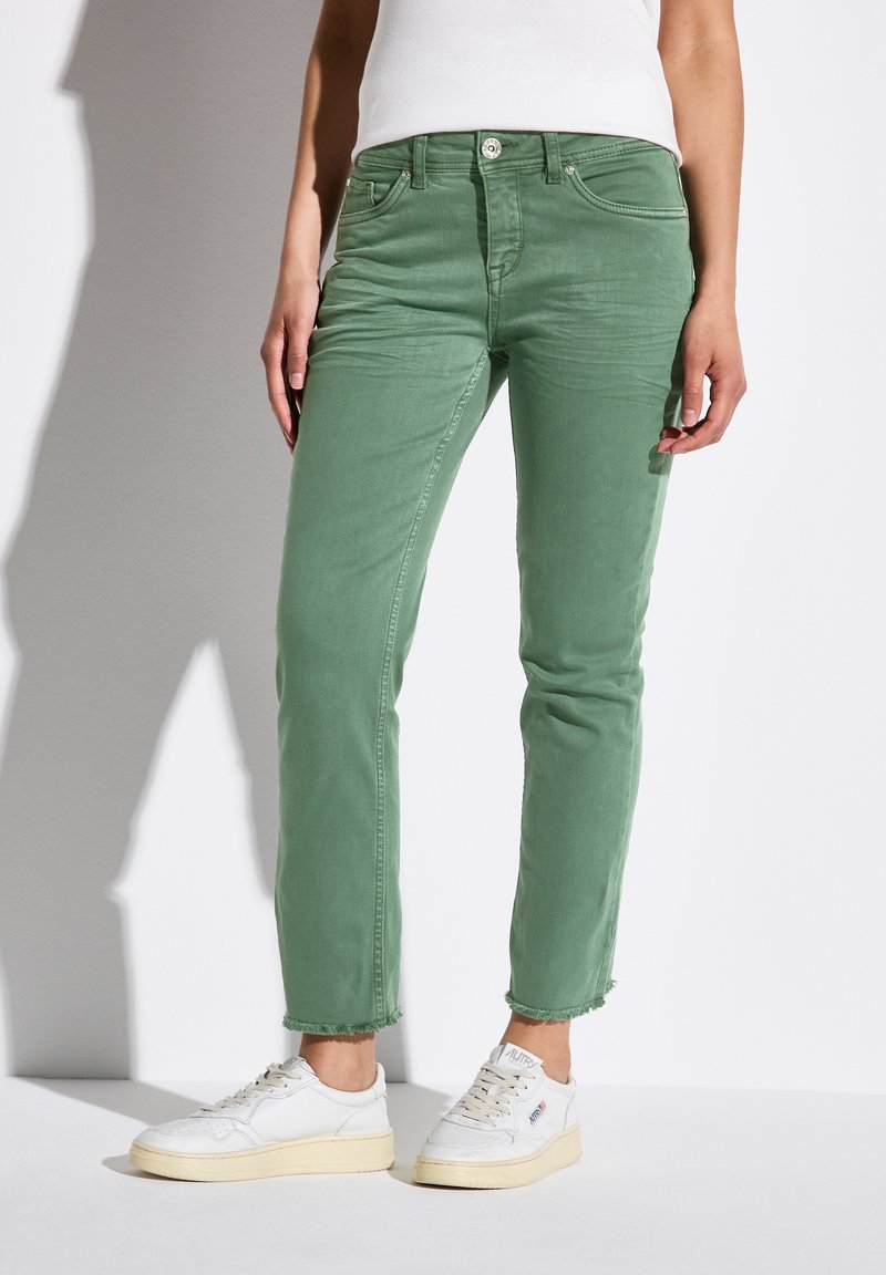 Gröna denimjeans med slim fit, ofärdig fåll, fem fickor och knappstängning. Matchas med vita sneakers.