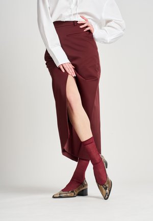 Falda lápiz burdeos con una abertura lateral, combinada con calcetines burdeos y zapatos de punta con diseño de estampado de serpiente y tacones cuadrados.