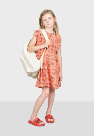 Robe corail avec impression graphique noire, cintrée à la taille. Sac à dos blanc avec un design texturé. Sandales à glisser rouges avec détail de logo.